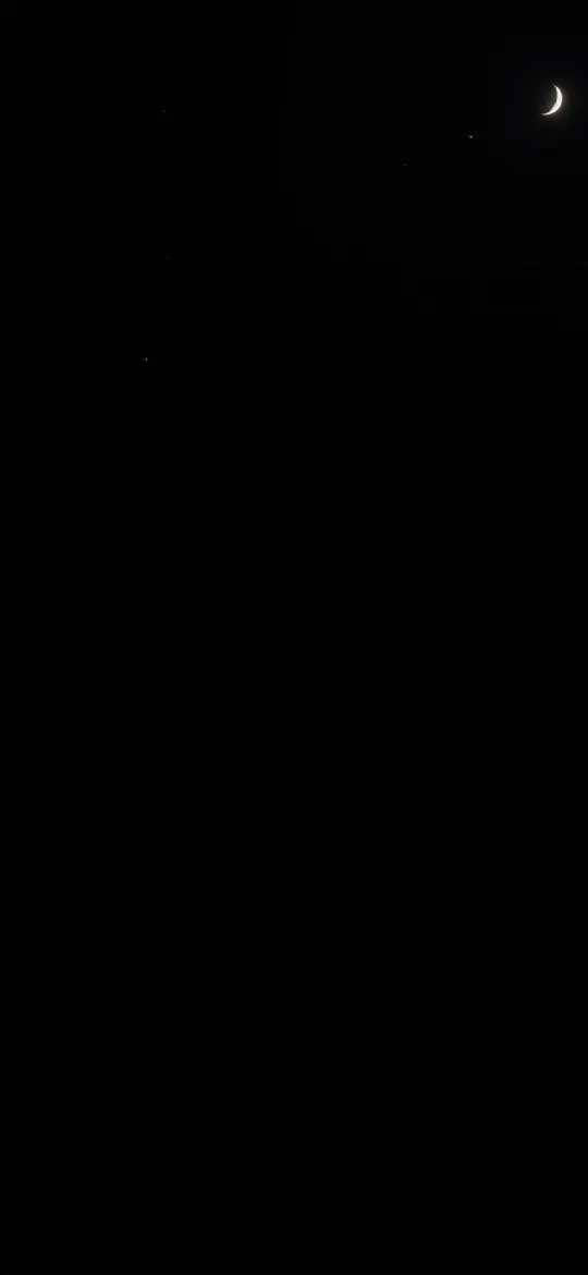 Thin crescent moon in the top corner of a black night sky with faint stars