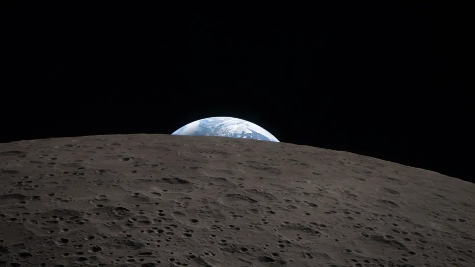 Earth setting behind the cratered grey surface of the Moon