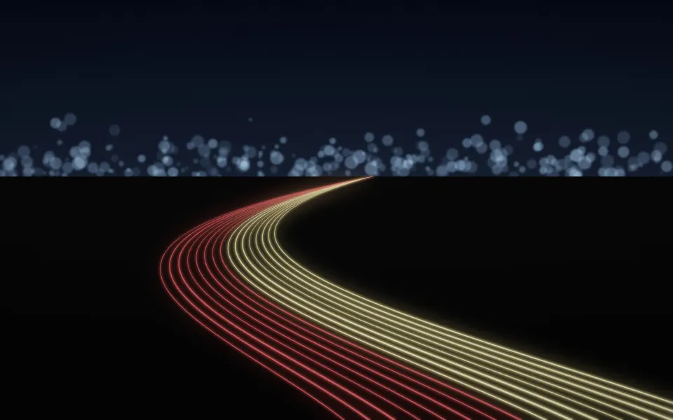 Freeway Light Ribbons: long streaks of red and gold light sweep across a dark freeway curve, the horizon lit by soft, blurred city lights, Mac wallpaper