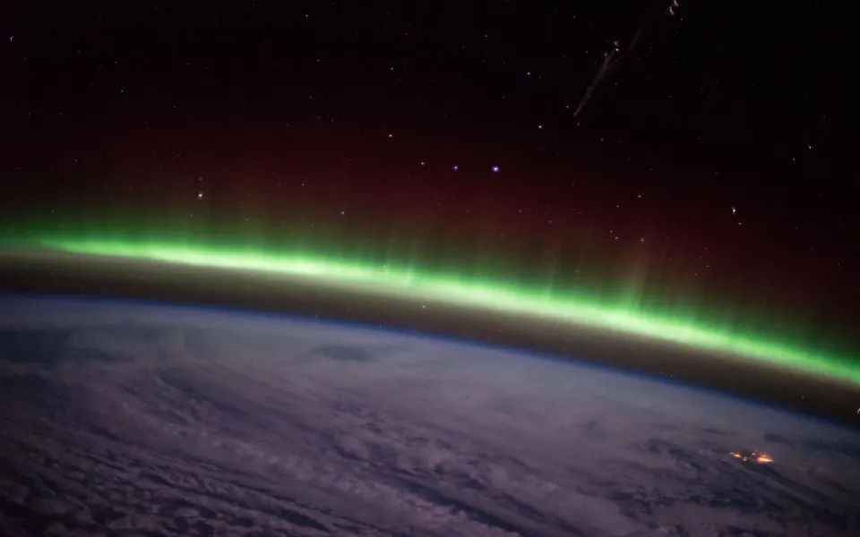 Thin green aurora along the horizon of Earth at night from space