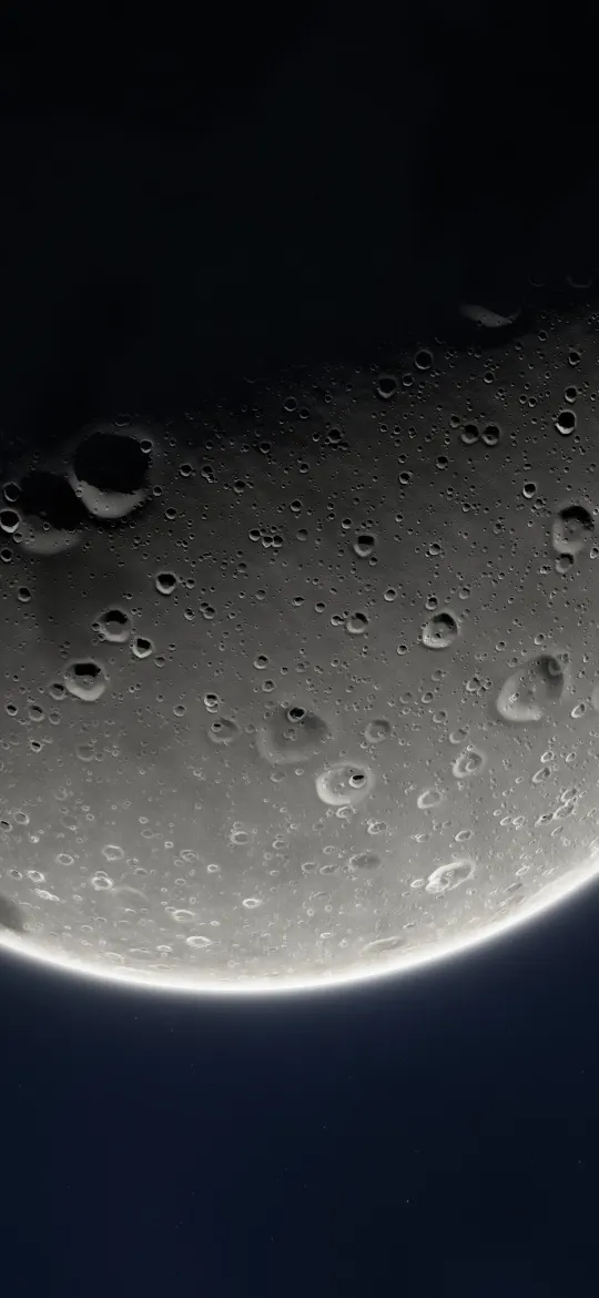 Huge Moon Rim Glow: a huge cratered moon fills the screen at an angle, lit from below so a thin bright rim glows against the dark sky, iPhone wallpaper