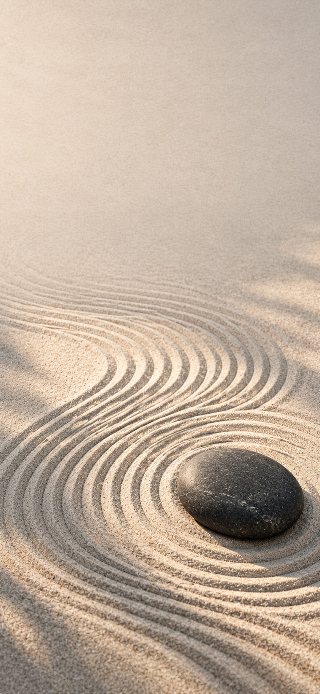 Smooth dark stone in raked sand ripples in a Japanese zen garden