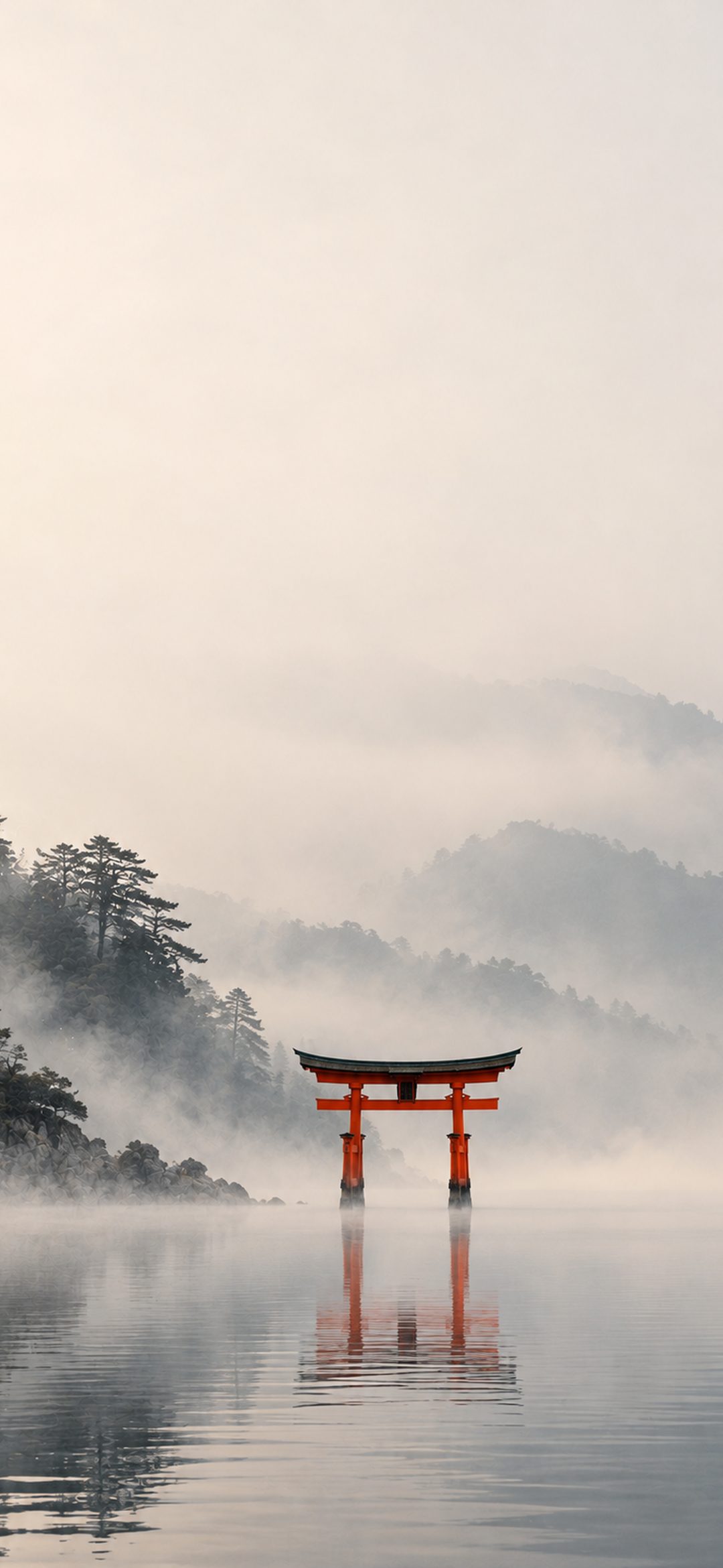 Red torii gate standing in a calm misty lake below pine-covered hills