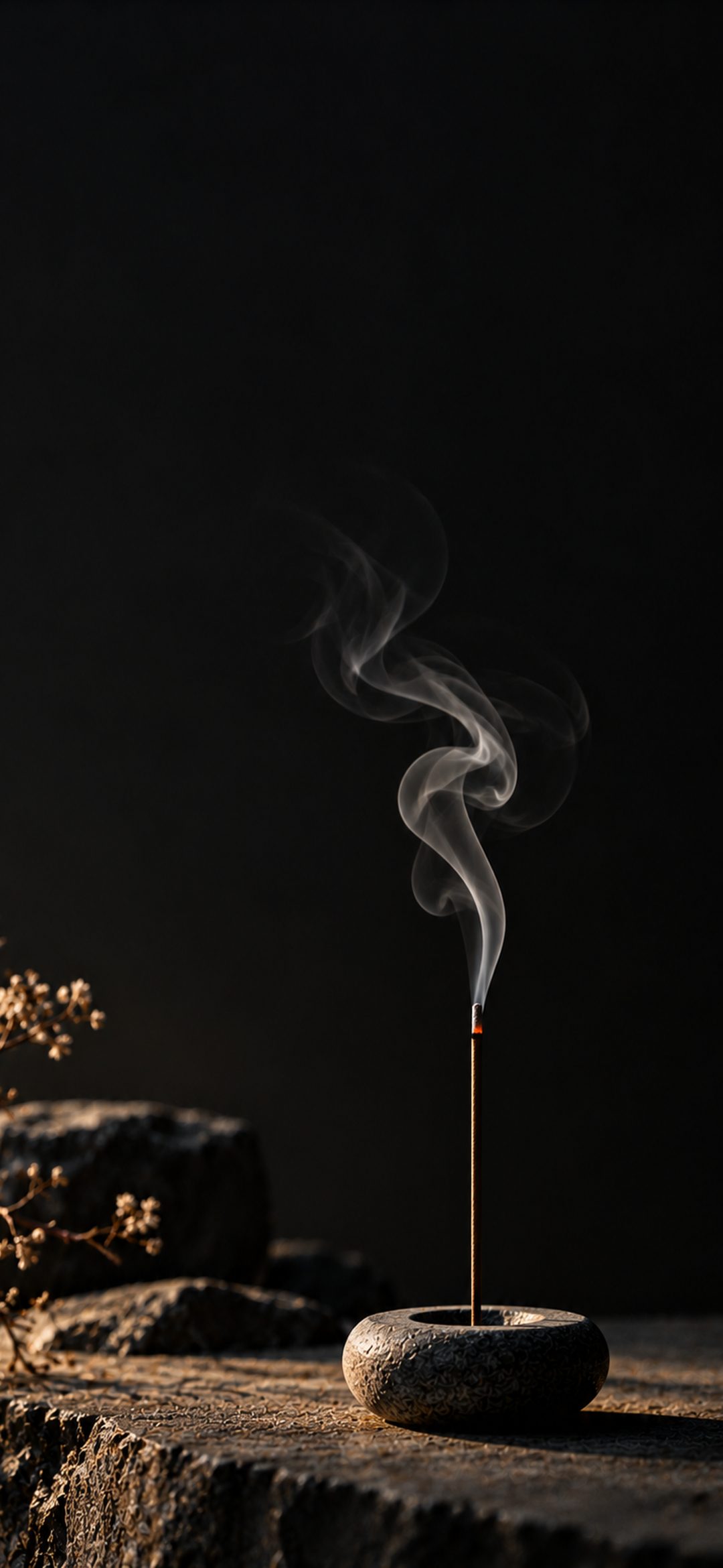 Thin incense stick in a dark stone holder with delicate white smoke curling upward against a black background.