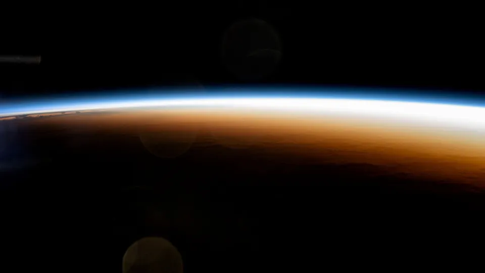 Thin glowing band of sunrise on Earth's horizon against black space