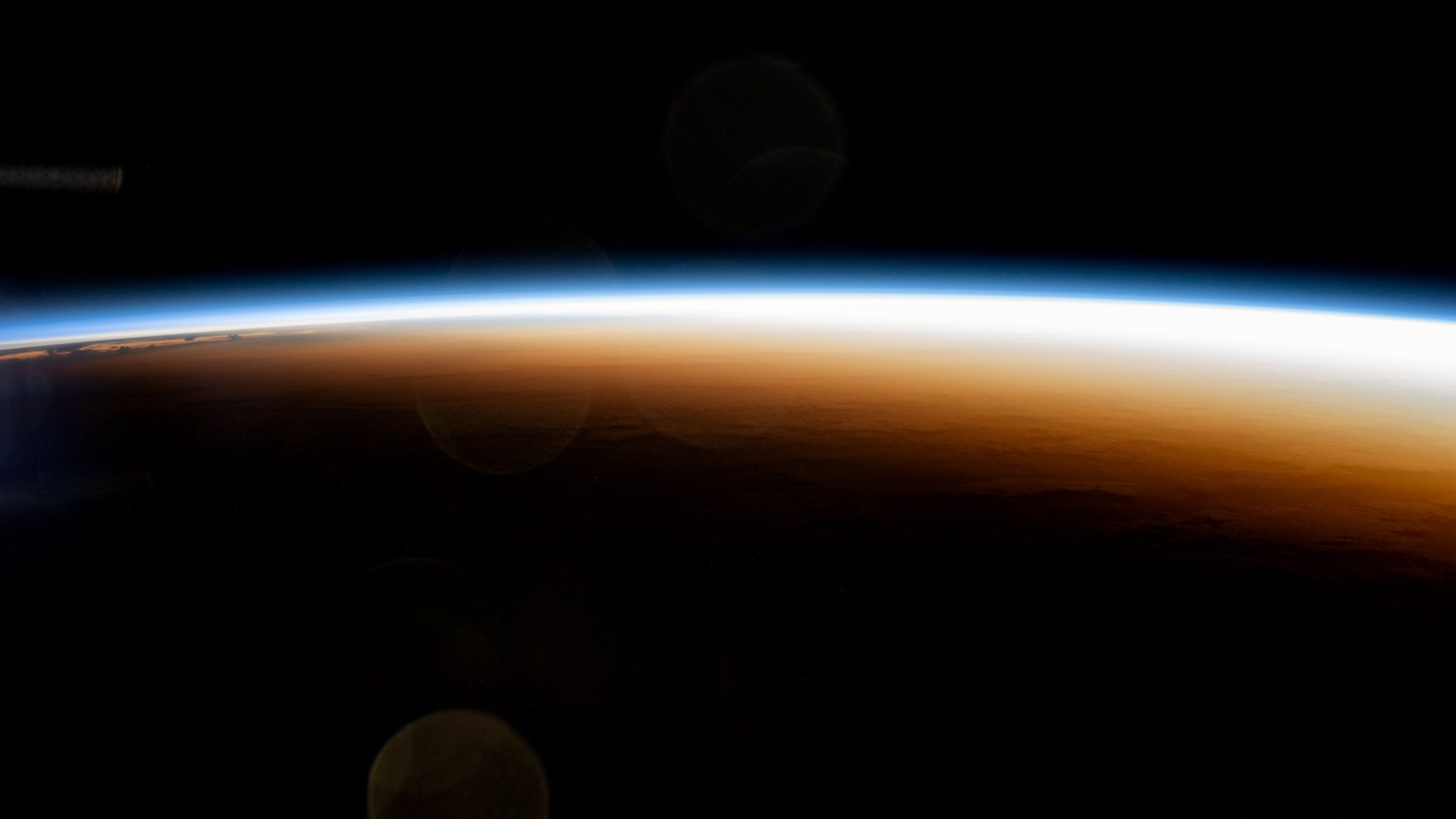 Thin glowing band of sunrise on Earth's horizon against black space