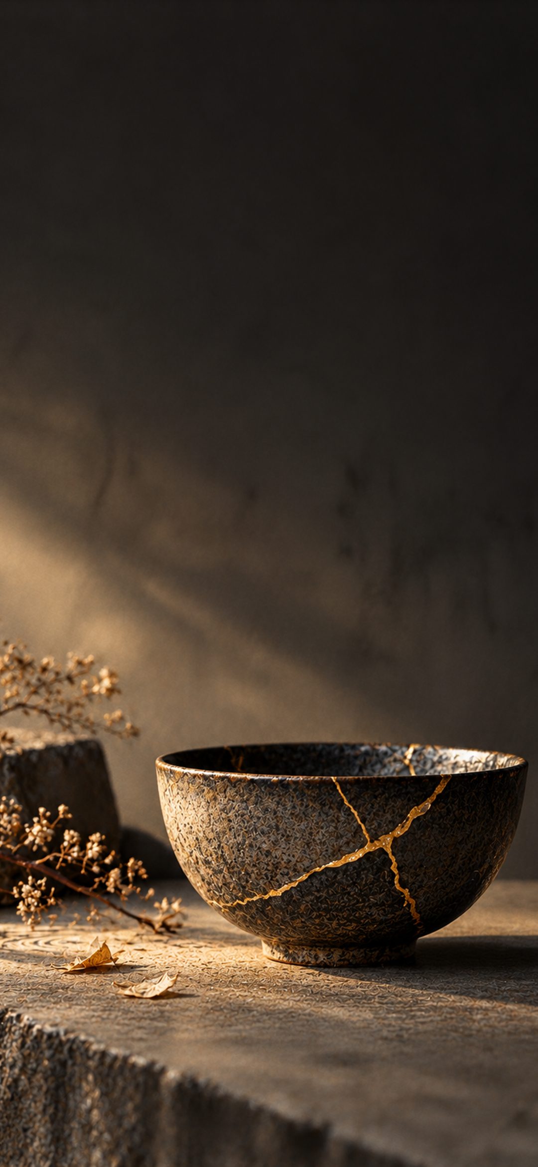 Dark ceramic bowl repaired with golden kintsugi cracks on a textured stone surface under warm side lighting